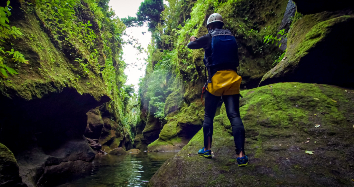 A man stands in a green moss covered canyon taking a photo in Dominica