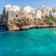 The white-washed cliff buildings stick out over the blue ocean of Polignano a Mare