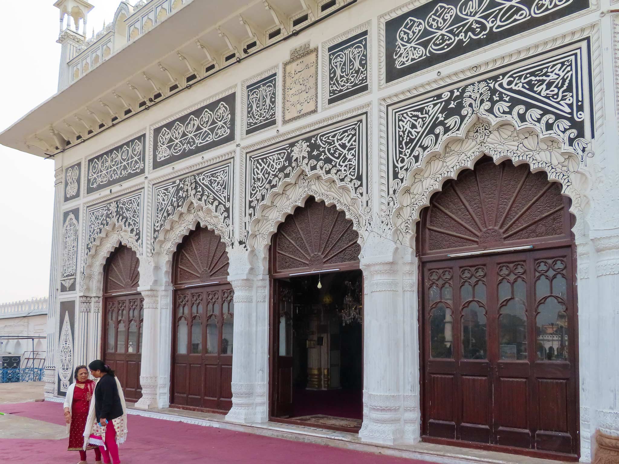 Arched door ways with intricate islamic design are met by a red carpet where two ladies talk