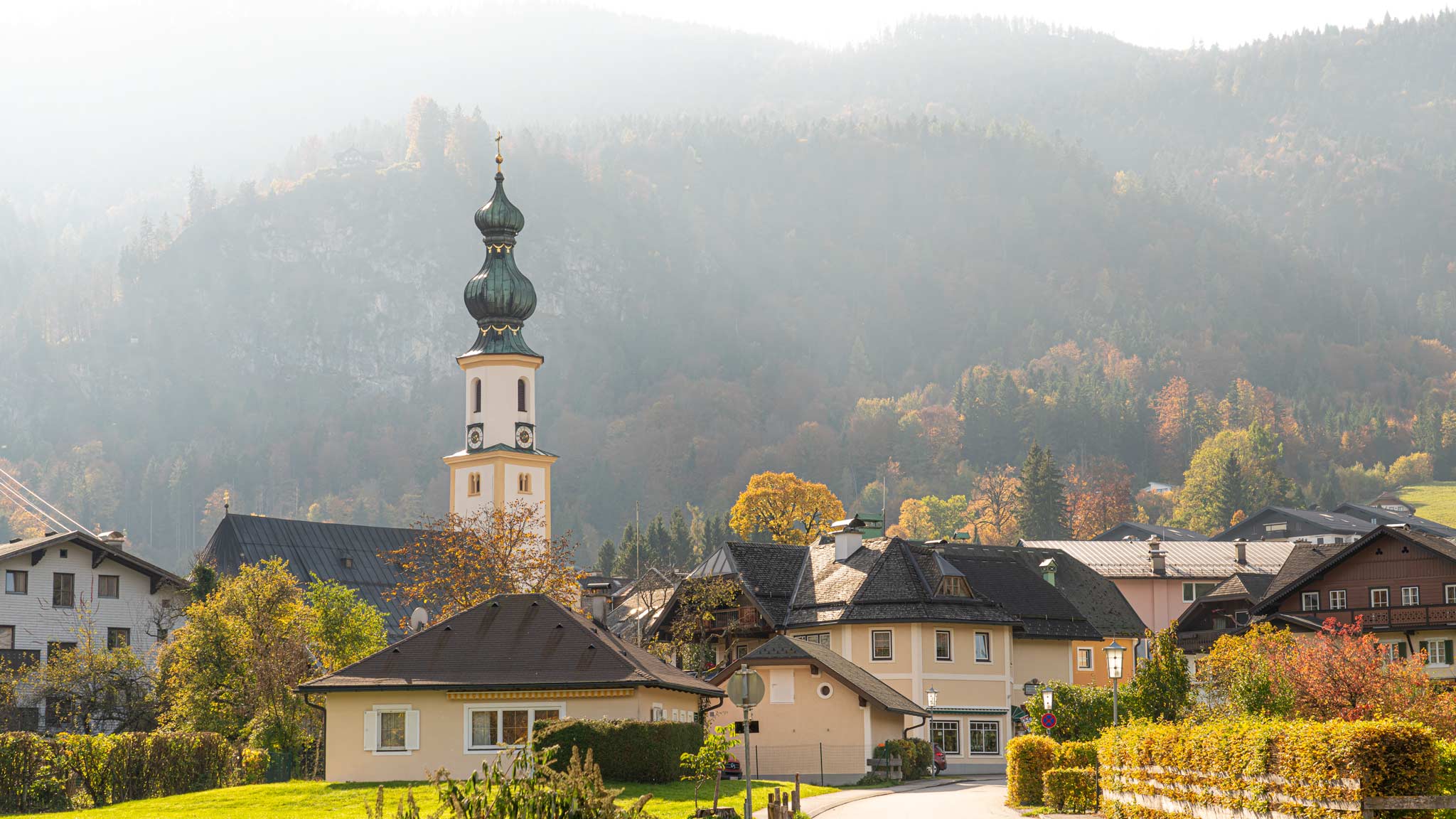 Beautiful mountain and lake views await in Saint Gilgen where a church spire stands infront of a towering mountain 