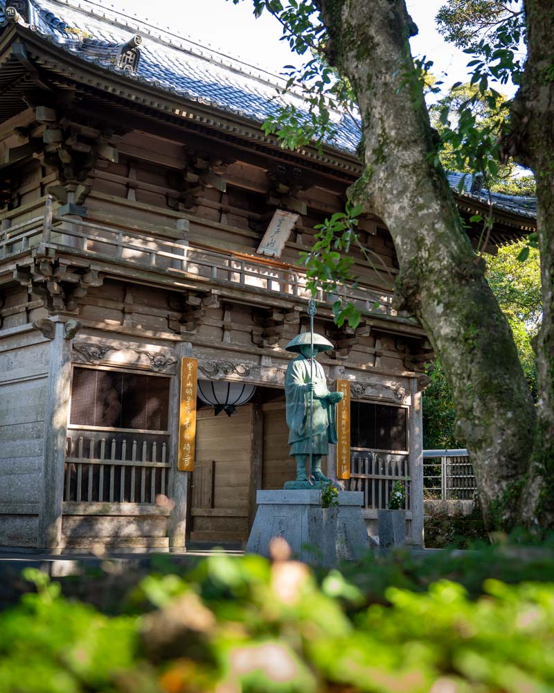 A statue stands in front of the wooden gates to a Kochi temple