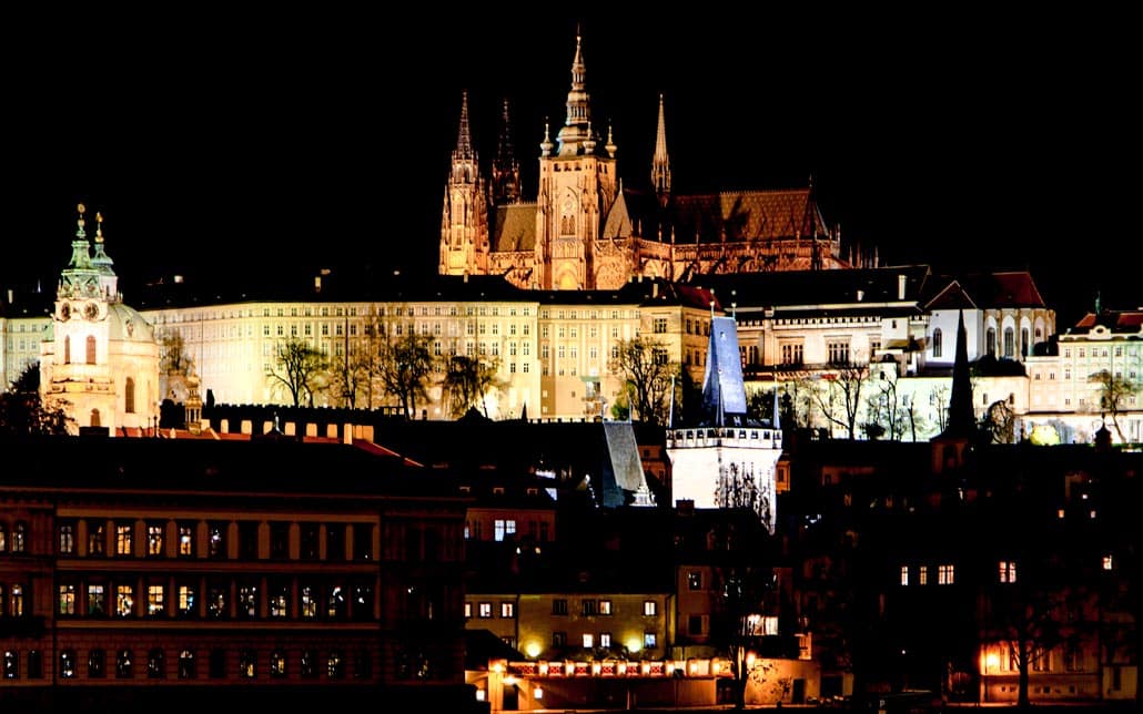 The capital city of Prague at night looking out on the castle from a river bridge