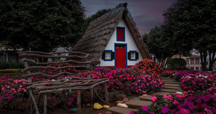 The traditional thatched houses of Santana, a pointed triangle shaped house with colourful blue and red windows and flowers outside