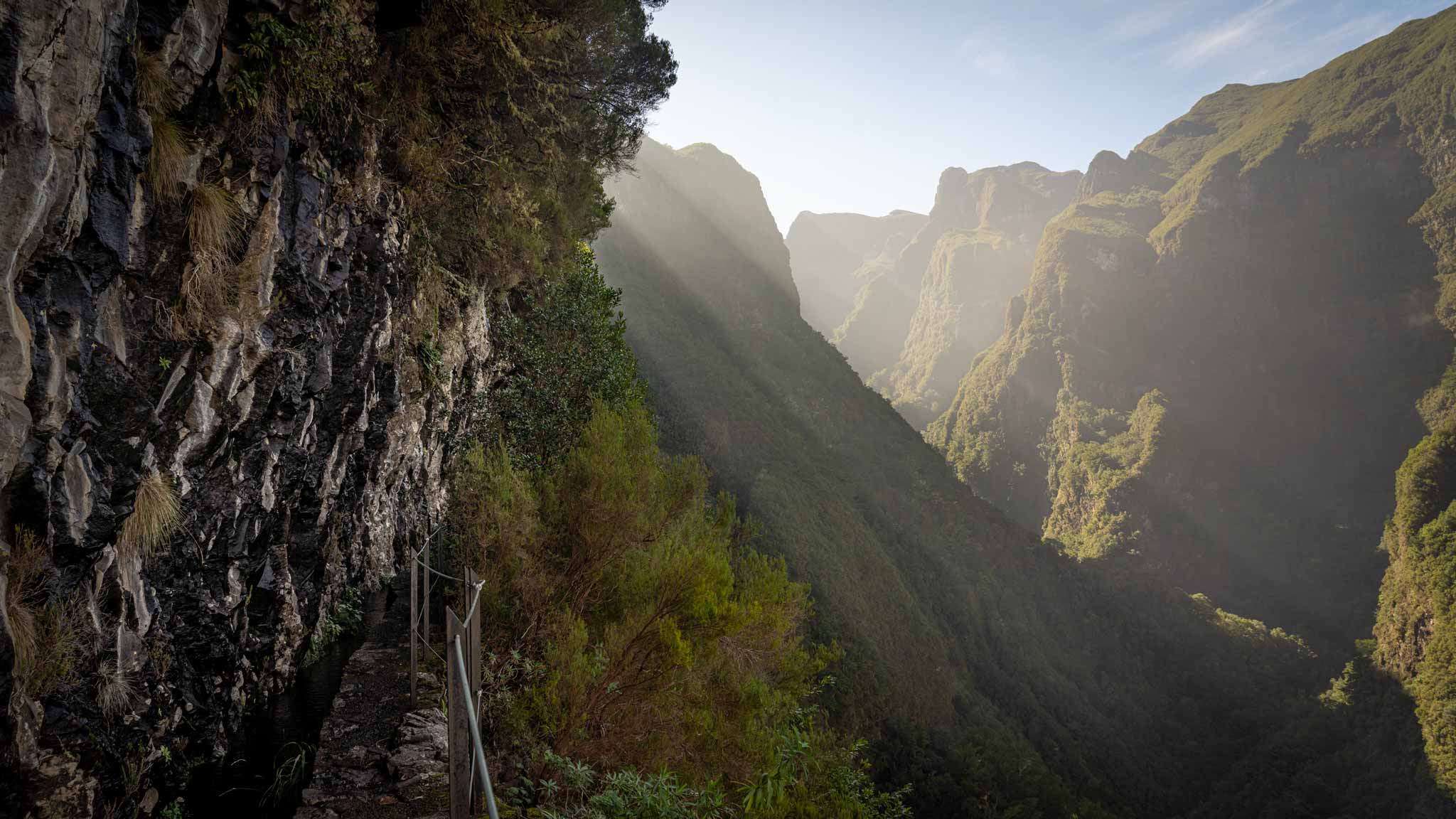 Rays of sun beam across the mountains and the Levada do Caldeirão Verde walking path is on the left