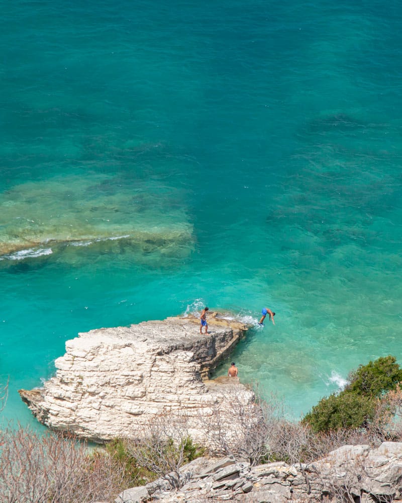 people dive into the water from a rock as Albania's beaches become a little more tempting from April