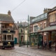 A vintage tram passes by old-style Victorian shops with wooden signs and porches