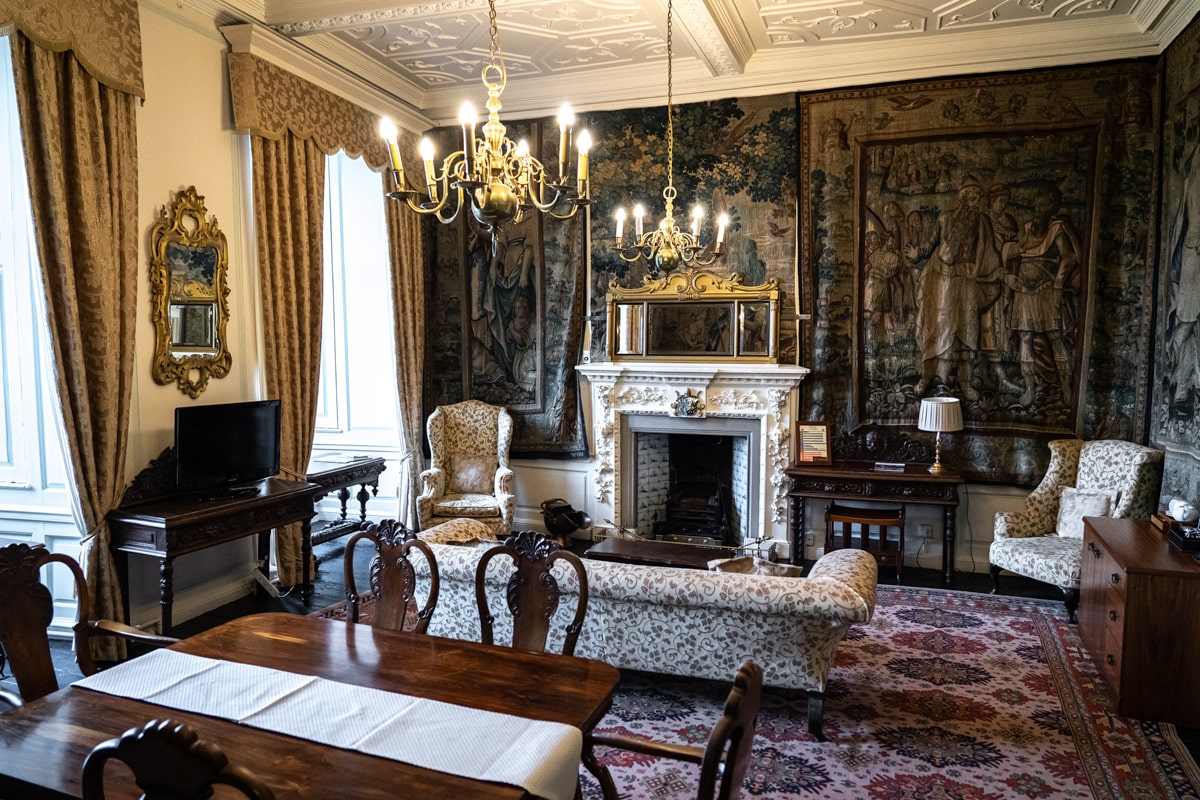 An opulent bedroom with green wall tapestries depicting historic scenes and a chandellier in Durham Castle