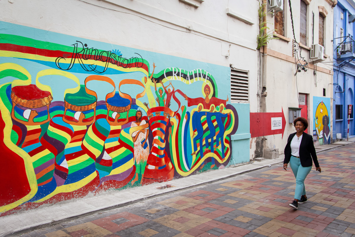 A mural with lots of colours reading Kingston with a woman walking past it